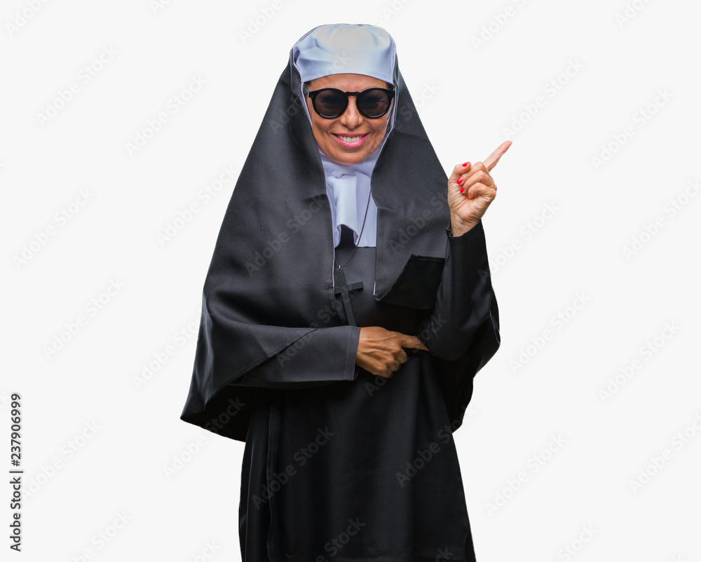 Middle age senior catholic nun woman wearing sunglasses over isolated background with a big smile on face, pointing with hand and finger to the side looking at the camera.