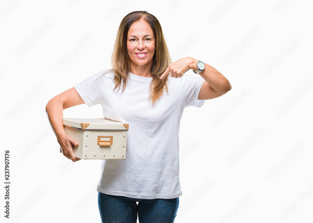 Middle age hispanic woman moving holding packing box over isolated background with surprise face pointing finger to himself Middle age hispanic woman moving holding packing box over isolated background with surprise face pointing finger to himself