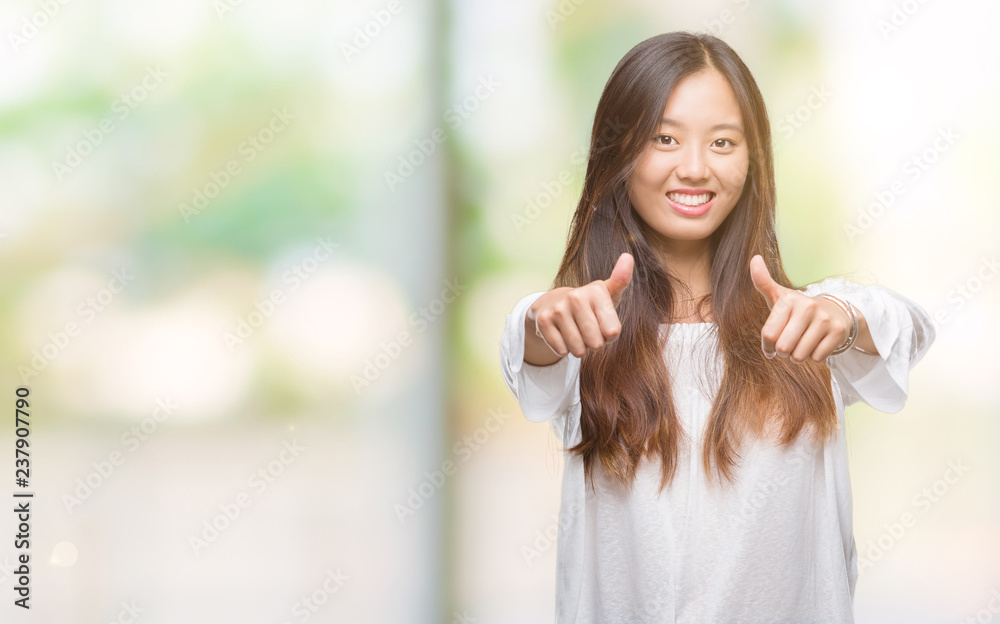 Young asian woman over isolated background approving doing positive gesture with hand, thumbs up smiling and happy for success. Looking at the camera, winner gesture.