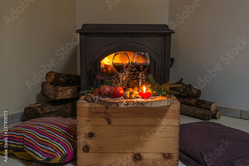 Cozy christmas holiday interiors: two coshion on the floor, two glasses of wine on the tree stump in front of the burning firplace photo