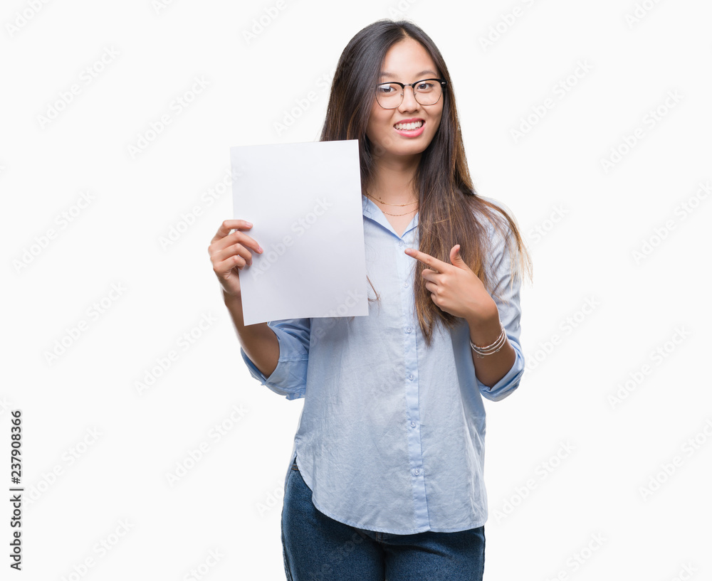 Young asian woman holding blank paper over isolated background very happy pointing with hand and finger Young asian woman holding blank paper over isolated background very happy pointing with hand and finger