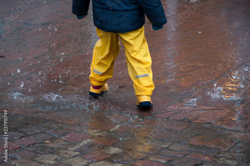 closeup of boy playing in puddle of water with yellow boots
