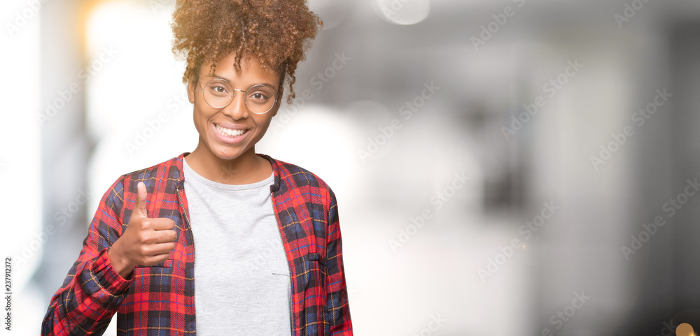 Fototapeta premium Beautiful young african american woman wearing glasses over isolated background doing happy thumbs up gesture with hand. Approving expression looking at the camera showing success.