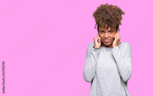 Beautiful young african american woman over isolated background covering ears with fingers with annoyed expression for the noise of loud music. Deaf concept.