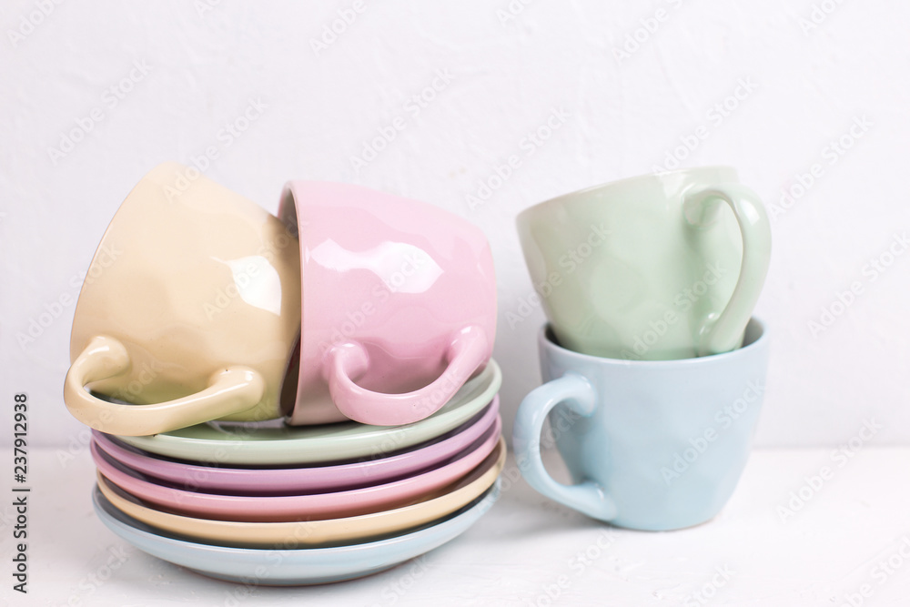 Pile of colourful tea cups and saucers on white textured background. Pile of colourful tea cups and saucers on white textured background.