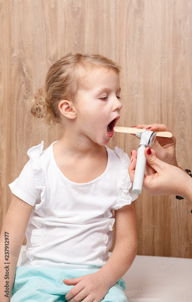 Child check up - doctor examining little girl throat using wooden tongue depressor and torch Child check up - doctor examining little girl throat using wooden tongue depressor and torch