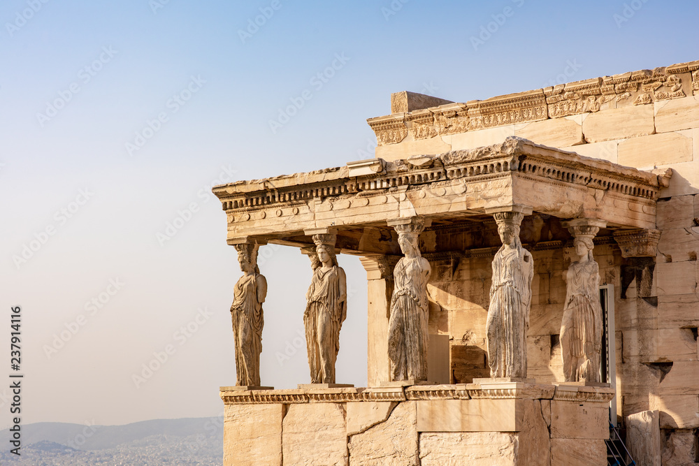 The ancient Erechtheion temple with the beautiful Caryatid pillars on the porch, with a golden glow at sunset, on the Acropolis in Athens, Greece.