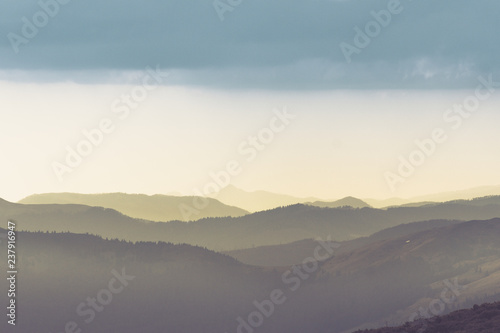 Majestic landscape of summer mountains. A view of the misty slopes of the mountains in the distance. Morning misty coniferous forest hills in fog and rays of sunlight.Travel background.