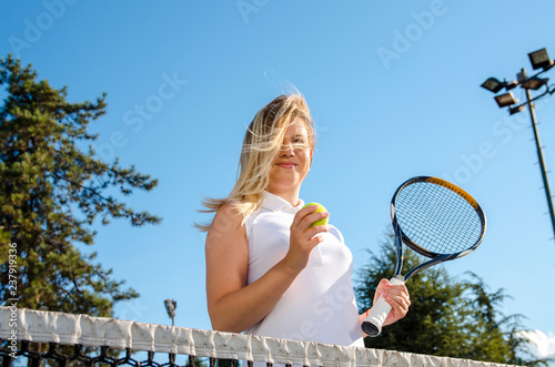 Female tennis player holding ball and racket by the net  © phoenix021