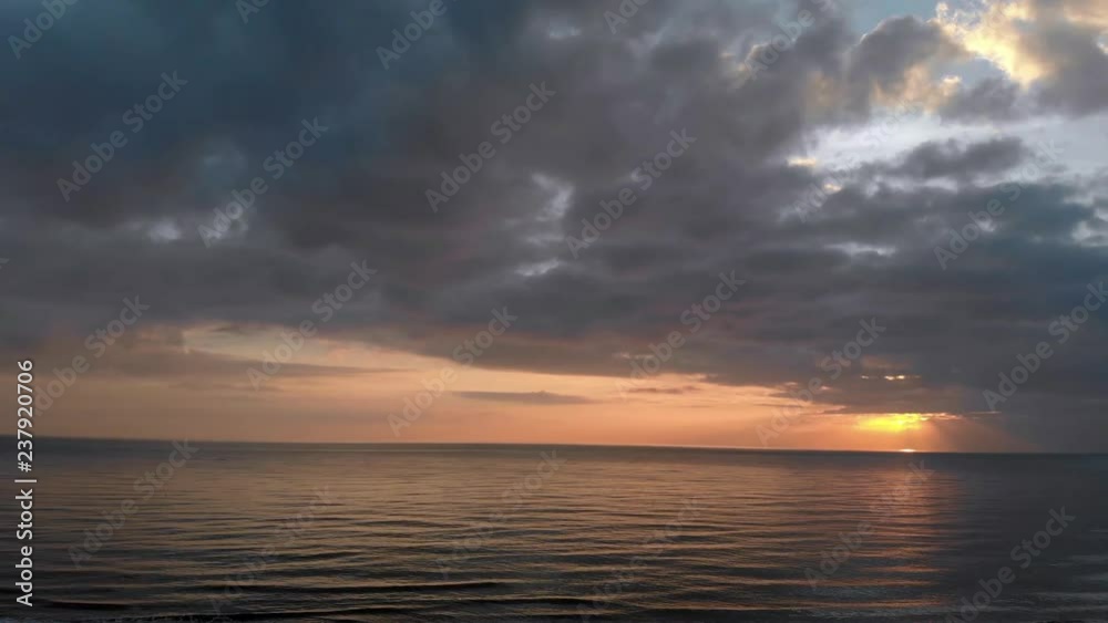 Aerial view up twilight sunset on ocean corrugated surface with sunbeams and orange light reflection and at horizon dark nimbostratus clouds Aerial view up twilight sunset on ocean corrugated surface with sunbeams and orange light reflection and at horizon dark nimbostratus clouds