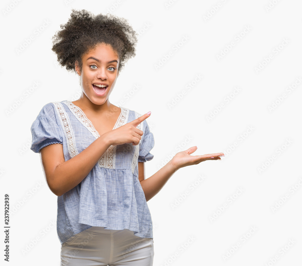 Young afro american woman over isolated background amazed and smiling to the camera while presenting with hand and pointing with finger. Young afro american woman over isolated background amazed and smiling to the camera while presenting with hand and pointing with finger.