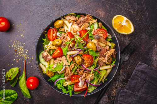 Tuna salad with pasta, olives and vegetables in black plate on dark background.