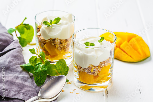 Greek yogurt mango granola parfait in a glass on white wooden background.