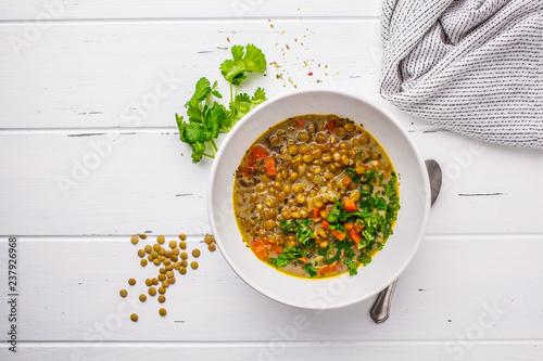 Homemade vegan lentil soup with vegetables and cilantro, white wooden background.