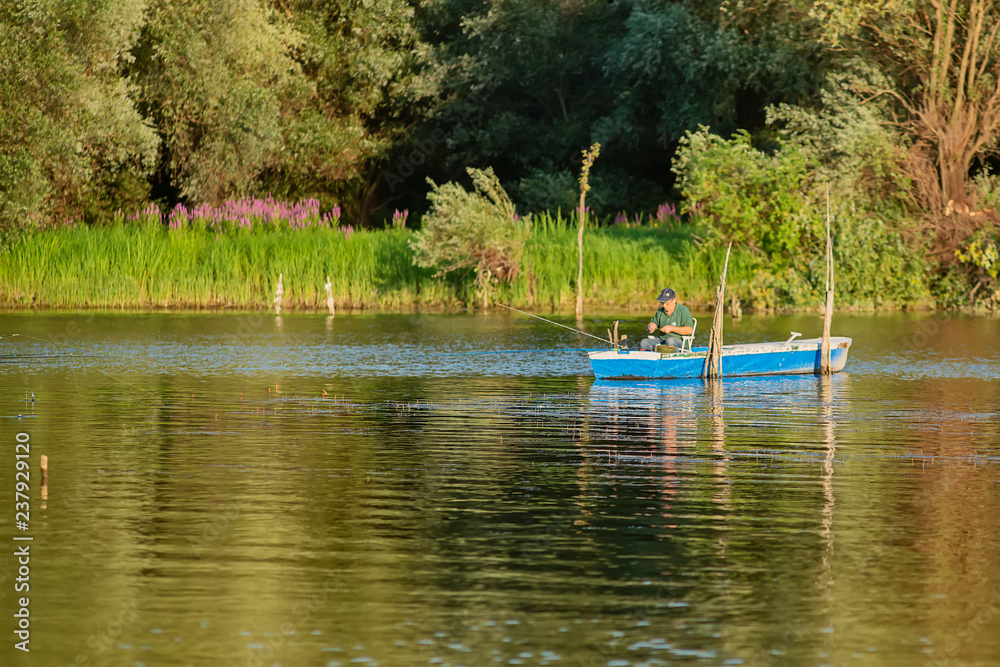Naklejka premium Novi Sad, Serbia - August 04, 2018: Danube island (Šodroš) near Novi Sad, Serbia. Fishermans sitting in boat and holding fishing rod.
