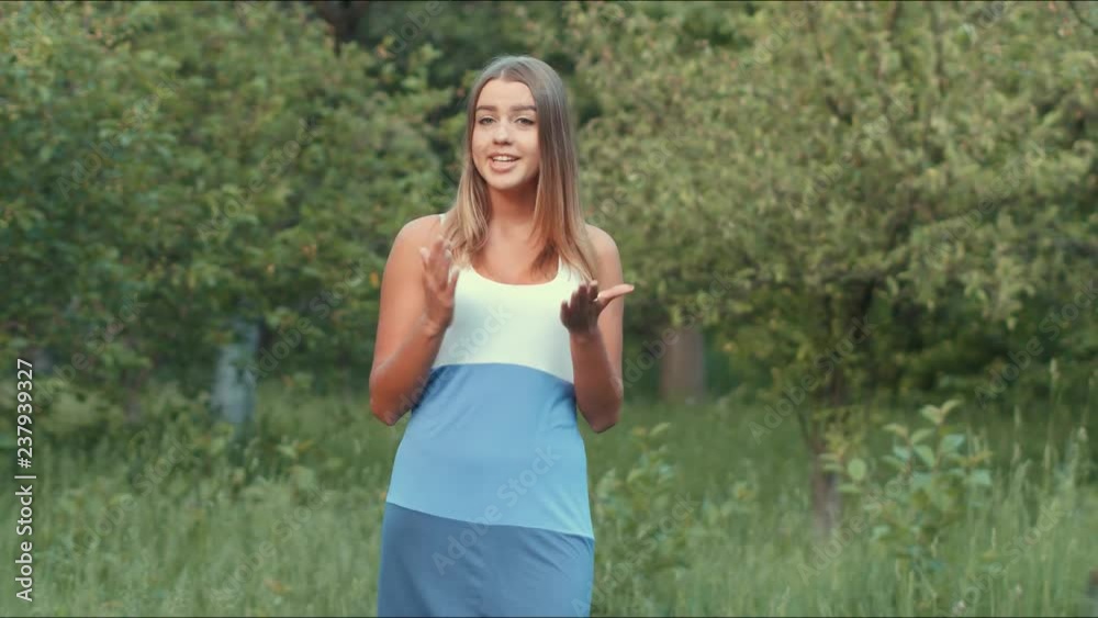 A magnificent Ukrainian girl of beautiful appearance is talking to the camera, summer time, the girl in the vest smiles and straightens her hair, the girl in the garden talks and behaves naturally A magnificent Ukrainian girl of beautiful appearance is talking to the camera, summer time, the girl in the vest smiles and straightens her hair, the girl in the garden talks and behaves naturally