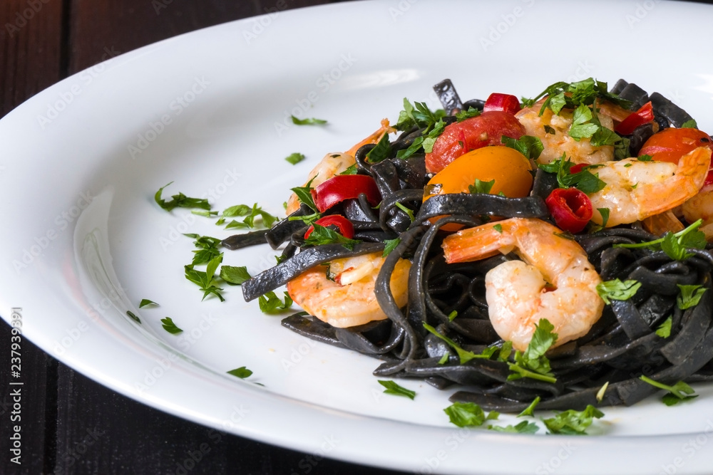 Black squid ink Fettuccine pasta with prawns or shrimps cherry tomatoes, parsley, chili in wine and butter sauce. Black squid ink Fettuccine pasta with prawns or shrimps cherry tomatoes, parsley, chili in wine and butter sauce.