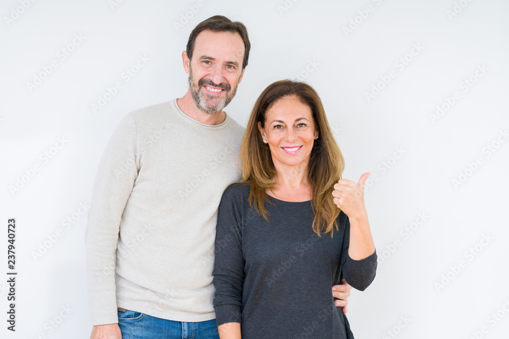 Beautiful middle age couple in love over isolated background smiling with happy face looking and pointing to the side with thumb up. Beautiful middle age couple in love over isolated background smiling with happy face looking and pointing to the side with thumb up.