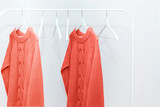 Living Coral knitted warm sweaters on hanger and many empty hangers. Color of the 2019 year.