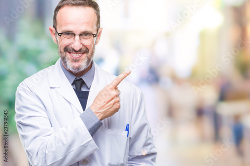 Middle age senior hoary professional man wearing white coat over isolated background cheerful with a smile of face pointing with hand and finger up to the side with happy and natural expression © Krakenimages.com