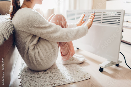Using heater at home in winter. Woman warming her hands. Heating season.
