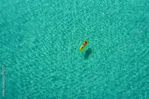 Aerial view of slim woman swimming on the swim mattress in the transparent turquoise sea in Seychelles. Summer seascape with girl, beautiful waves, colorful water. Top view from drone