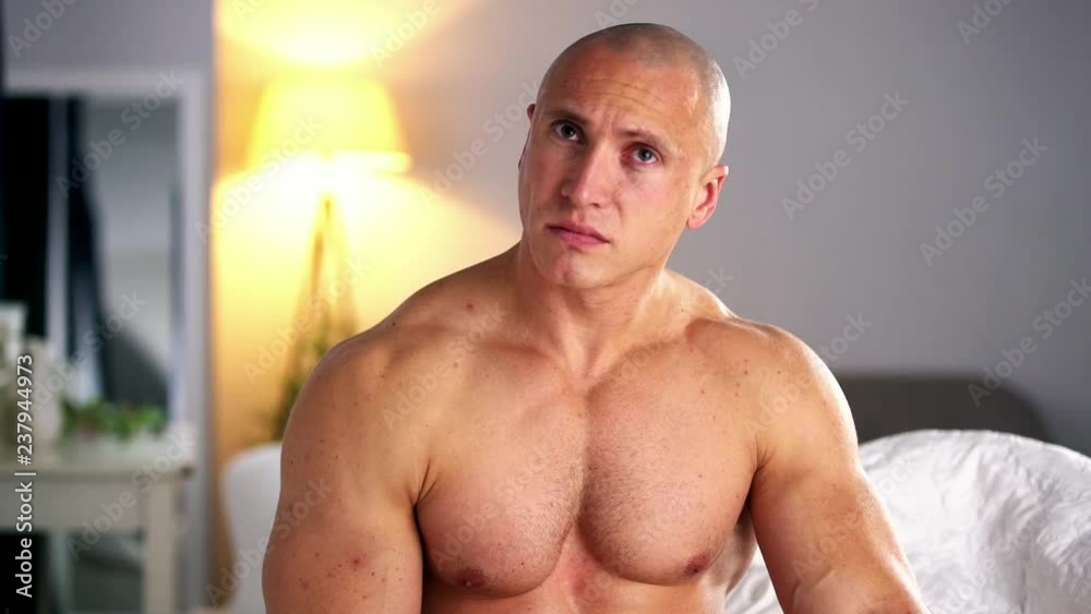 A naked bodybuilder in a bright room complains about health problems, a strong man has a headache, a sports guy with a naked torso clutches his head, a man hurts, a handsome powerful guy in bed