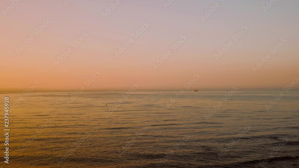 A Small Fishing Vessel Slowly Moving on Open Mediterranean Sea at Pastel Colored Sunrise. The Colors are Reflecting in the Ocean. A Small Fishing Vessel Slowly Moving on Open Mediterranean Sea at Pastel Colored Sunrise. The Colors are Reflecting in the Ocean.