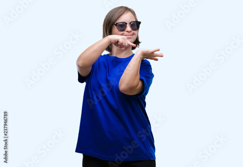Young adult woman with down syndrome wearing sunglasses over isolated background amazed and smiling to the camera while presenting with hand and pointing with finger. © Krakenimages.com