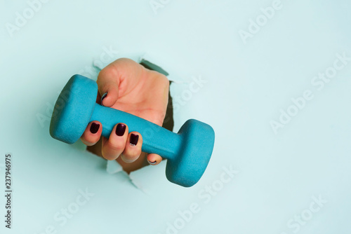 Woman hand holding blue dumbbell on blue background. Fitness, sport, healthy lifestyle, diet concept. Banner with copy space