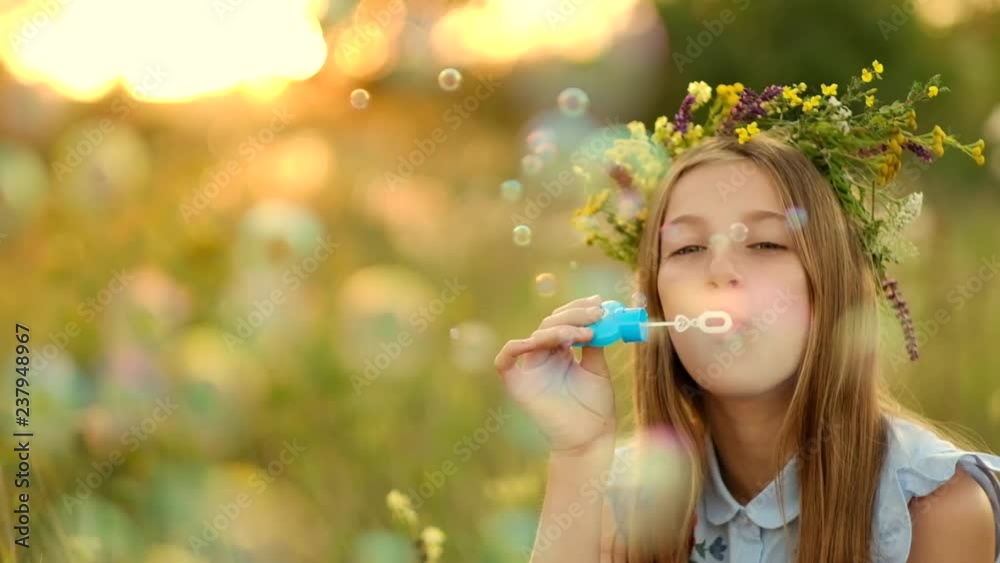 Girl is blowing bubbles on the meadow and during sunset