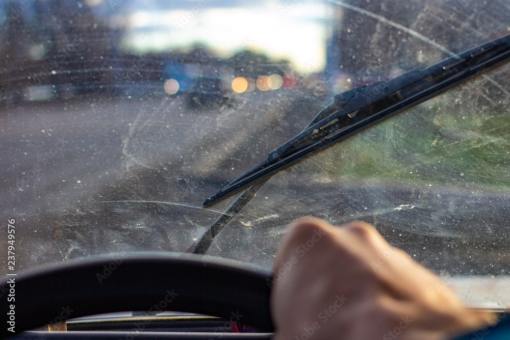 dirty scratched car windshield with wiper through blurred steering