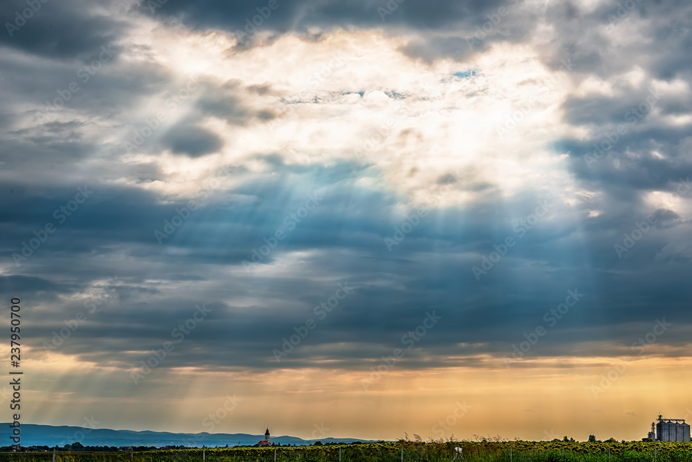 Naklejka premium View from the highway to Kovilj city and the mountain Fruska Gora from Serbia. Black clouds over the urban city with sun rays penetrating through.