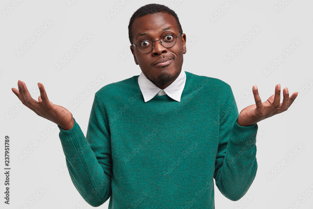 Hesitant uncertain man with dark skin, shrugs shoulders in bewilderment,  has doubtful look, spreads palms, dressed in green sweater, isolated over  white background. People and hesitation concept Stock Photo | Adobe Stock