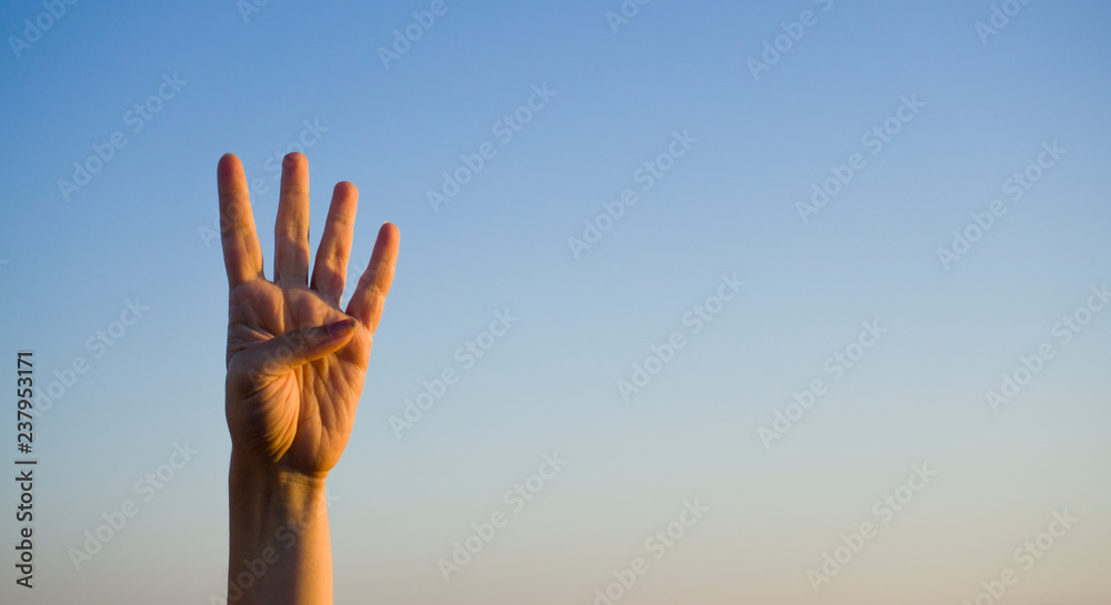 Hand doing / showing number four gesture symbol on blue summer sky nature background. Gesturing number 4. Number four in sign language. Fourth and counting down four concept. Four fingers up.