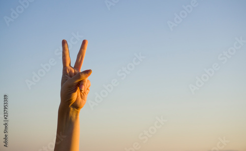 A hand doing number two gesture on blue background. Gesturing number 2. Peace or victory symbol. Number two / letter V in sign language. Being second concept. Hand counting two. Space for ad text. 