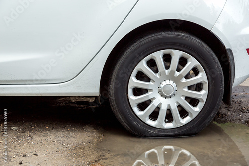 A dirty white car is standing in a puddle of water, a close-up of a wheel with a reflection of a wheel in a puddle.