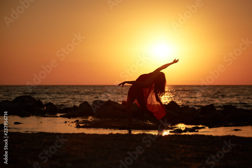 girl gymnast in red dress dancing on the beach at sunrise