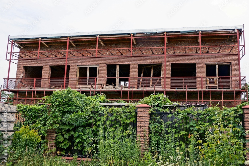 Fototapeta premium large unfinished house behind the fence with green vegetation
