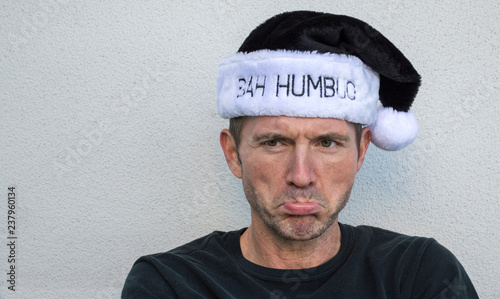 pouting Caucasian man wearing a black and white fur hat displaying the words Bah Humbug on the brim, with copy space photo