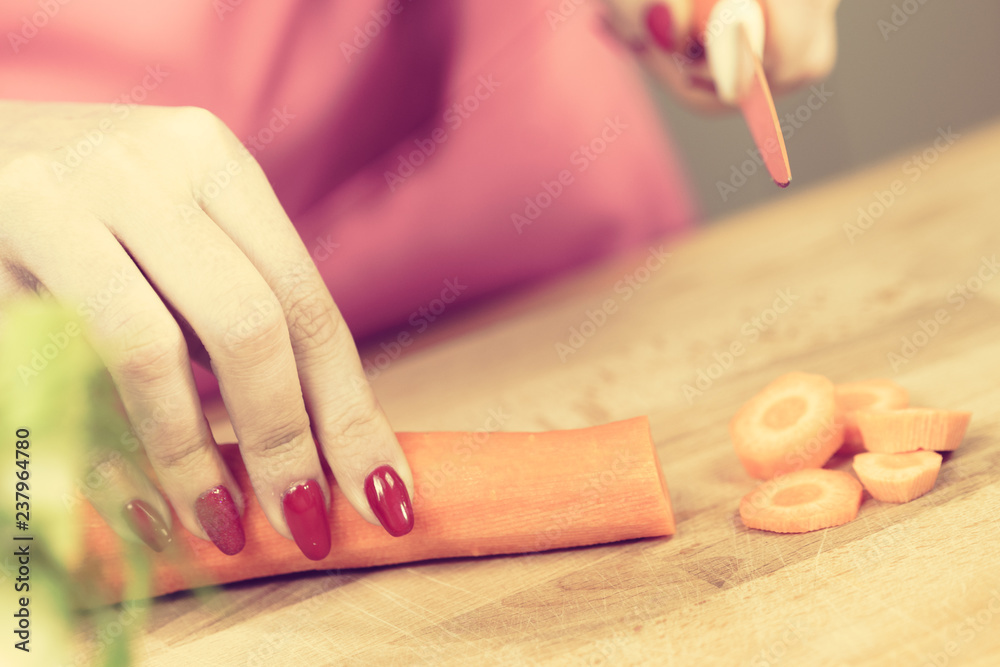 Woman cutting carrot on kitchen board Woman cutting carrot on kitchen board