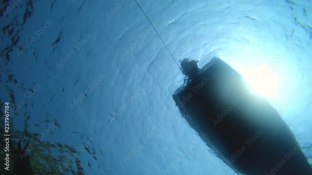 Underwater shot of man swimming diving with fins and mask under boat floating.