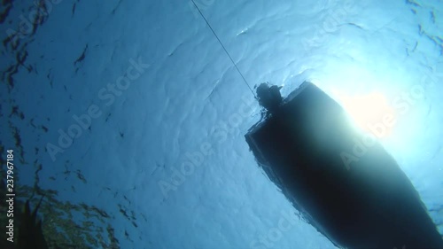 Underwater shot of man swimming diving with fins and mask under boat floating.