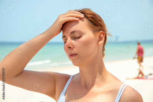 Sunstroke woman on sunny beach. Woman with headache. Hot sun danger. Health problem on holiday.