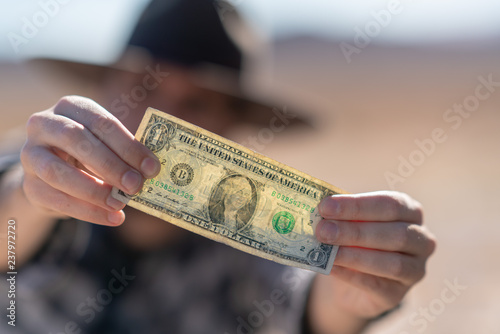 Cowboy with grey hat, moustache and checkerboard shirt holding a dollar note, close up