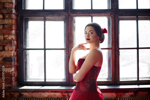 Portrait of a beautiful young woman dancer in a red dress near the window.