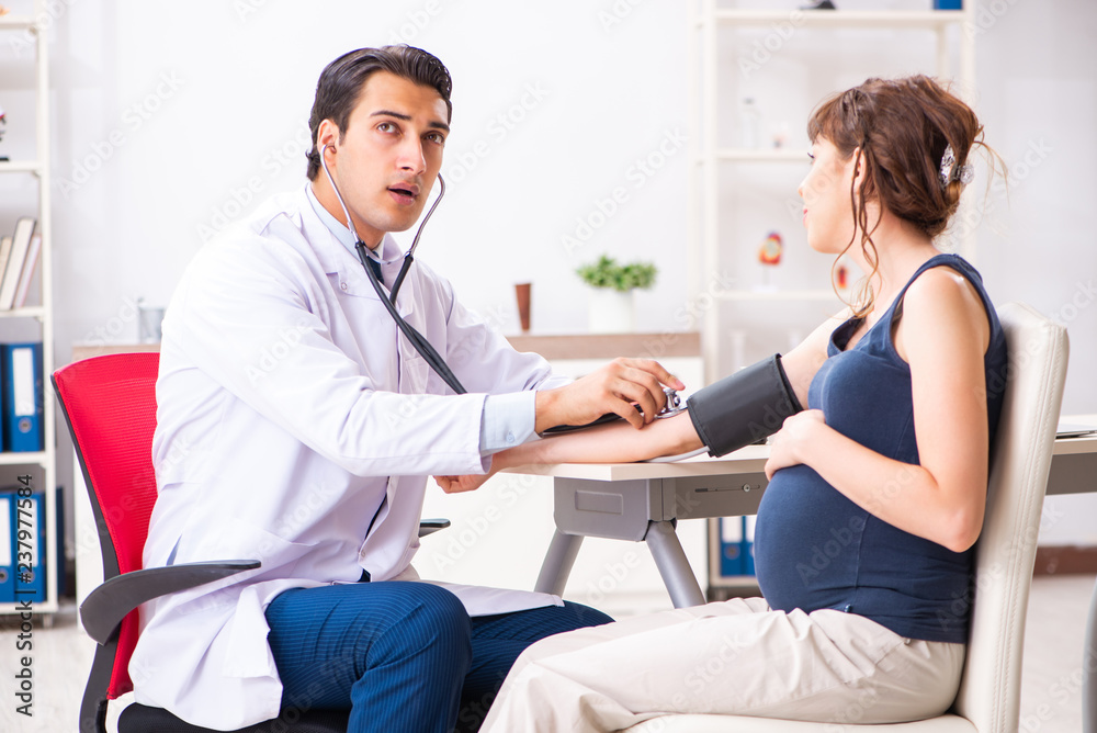 Fototapeta premium Young doctor checking pregnant woman's blood pressure