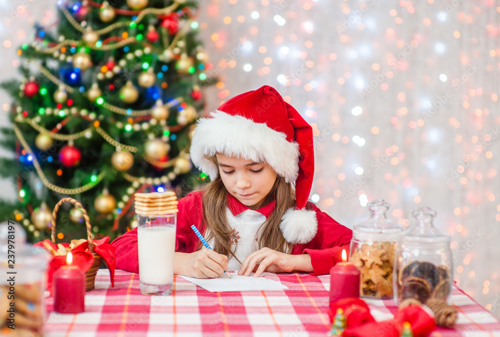 Little girl in red christmas hat writes letter to Santa Claus