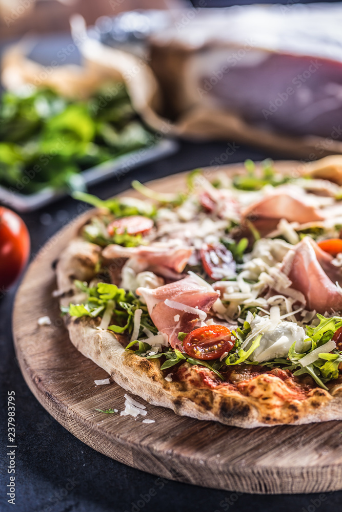 Italian pizza with prosciutto arugula tomatoes and parmesan on wooden round board