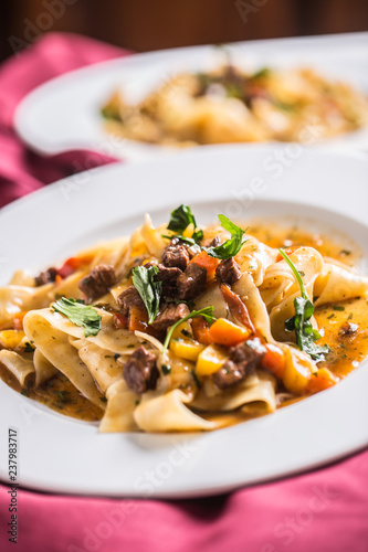 Idalian pasta pappardelle with beef ragout on white plate.